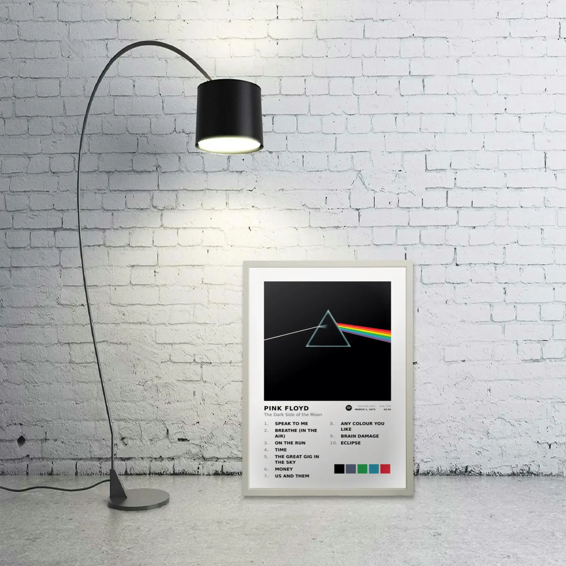 Pink Floyd album art metal print leaning against a white brick wall beside an arc lamp