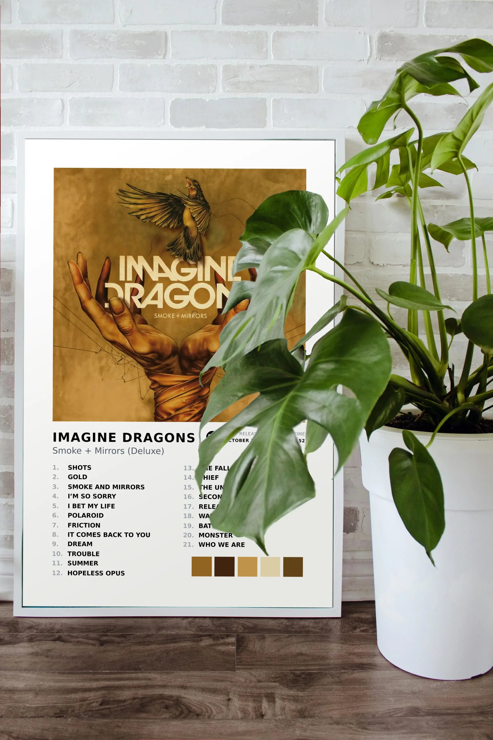 Imagine Dragons album metal print propped against a white brick wall with a monstera plant